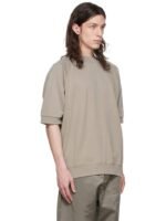 A person with long hair is wearing an Essentials Taupe Cotton Sweatshirt and matching pants. They are standing against a white background, looking to the side.