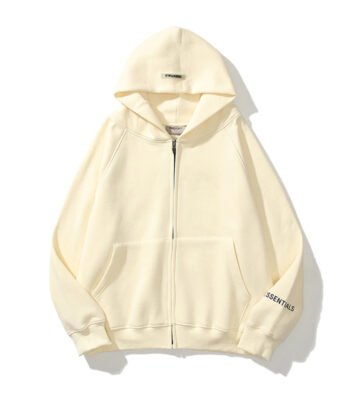 A cream-colored zip-up hoodie with a hood, called the Essentials Reflective Print Zip-up Oversized Cream Hoodie, featuring the word ESSENTIALS on the right sleeve. It is laid flat on a white background.