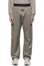 A person wearing the Essentials Taupe Nylon Lounge Pants with an elastic waistband featuring a label, along with a matching long-sleeve top. The pants and top create a casual, sporty look paired with white sneakers.