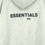 Essentials Fleeces Thick Light Gray Hoodie featuring black text reading "ESSENTIALS" prominently on the back with "GOD" in smaller letters below.