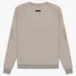 The FG Essentials Crewneck Sweatshirt 'Core-Heather' is showcased on a white background. It boasts a light beige color with long sleeves adorned with subtle G letters on each arm. The sweatshirt's minimalistic design is complemented by a small black tag near the back neckline.