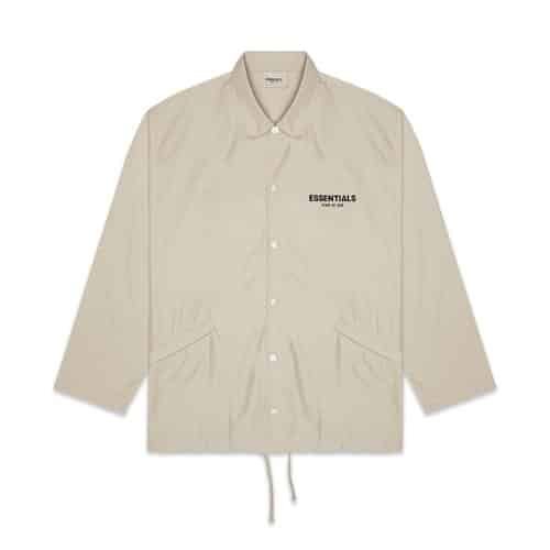 The Fear of God Essentials Coach Olive Jacket is a pale beige, long-sleeved jacket featuring a button-up front and two side pockets, with the word "ESSENTIALS" printed in black on the upper left chest area.